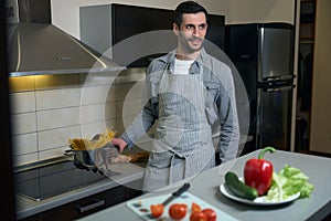 Male in casual clothes and chefs apron is engaged in cooking
