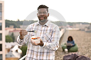 Male in casual shirt, with fork in hand and vegetable salad in bowl.