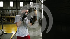 Male, caucasian boxer practicing kicks in black gloces using a puching bag made from car tyres. Old style boxing studio