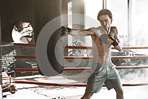 Male Caucasian boxer punching a boxing bag in boxing studio with bright light. Sport, fitness, healthy body, boxing