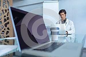 Male Caucasian doctor using laptop at table in the hospital