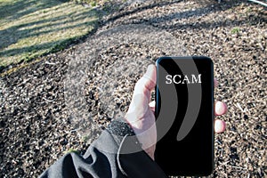 Male Caucasian hand in black jacket outdoors holding smartphone that says call is from spam.