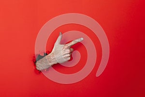 Male caucasian hand through a hole pointing against a red background