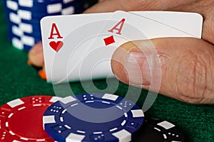 A male Caucasian hand Showing a Pair of Aces in the hole, Hearts and Diamonds, a standard red and white deck of cards with blue,