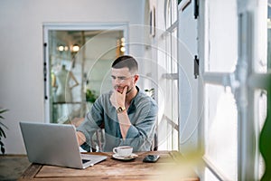 A male caucasian, Handsome Freelancer bearded man in t-shirt taking notes at laptop sitting at desk. freelance concept