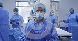 Male caucasian surgeon wearing face mask, surgical cap and protective clothing in operating theatre