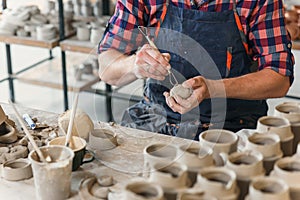 Male ceramist in the uniform works with clay at pottery workshop.