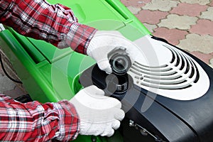 Male Checking the fuel level in lawn mower. A green lawnmower. Gardening. Maintenance of equipment