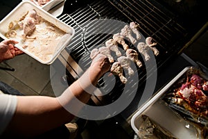 Male chef accurate puts marinated chicken legs to barbecue grill