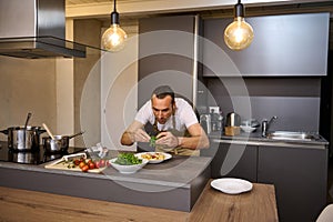 Male chef adding fresh green arugula leaves to Italian pasta with tomato sauce, garnishing the dish. A man preparing