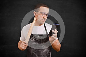 Male chef in apron using phone on dark background. Cooking concept