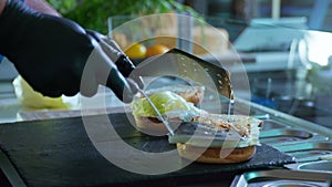 Male chef in black gloves cooks juicy tasty burgers with cheese and meat on a cutting board, stirring ingredients with