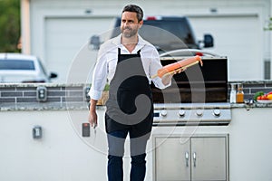 Male chef in cook apron grilling and barbequing salmon fish in garden. Handsome man preparing barbecue salmon fillet