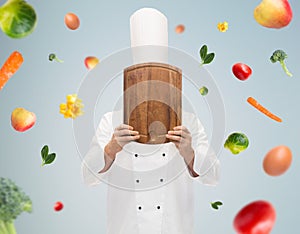 Male chef cook covering face with cutting board