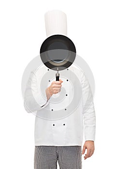 Male chef cook covering face with frying pan