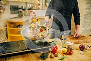Male chef cooking meat with vetables into the pan