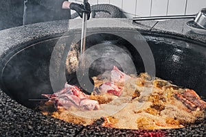 male chef cooks lamb meat in a boiling cauldron for oriental Uzbek pilaf in kitchen in Uzbekistan in Tashkent