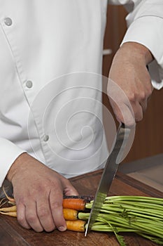 Male Chef Cutting Carrots On Wooden Board