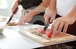Male chef cutting meat on wooden board at table