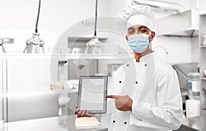 Male chef in face mask with tablet pc at kitchen