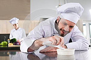 Male chef garnishing dish on restaurant kitchen in front of