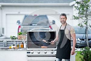 Male chef grilling and barbequing in garden. Barbecue outdoor garden party. Handsome man preparing barbecue meat
