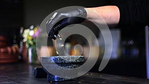 Male chef hand in black glove sprinkling seeds seasoning to marble bowl for mixing side view slowmo