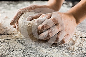 Male chef hands knead dough with flour on kitchen table