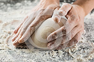 Male chef hands knead dough with flour on kitchen table