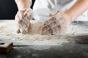 Male chef hands knead the dough with flour on the kitchen table