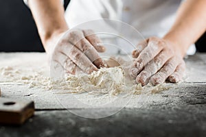 Male chef hands knead the dough with flour on the kitchen table