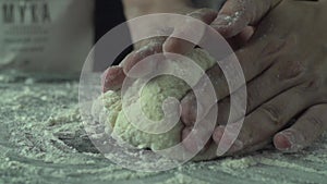 Male chef hands knead dough with flour on kitchen table