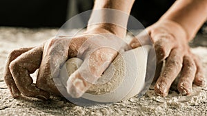 Male chef hands knead dough with flour on kitchen table