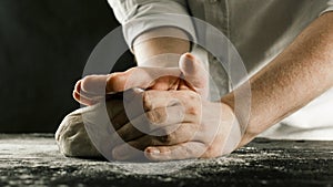 Male chef hands knead dough with flour on kitchen table