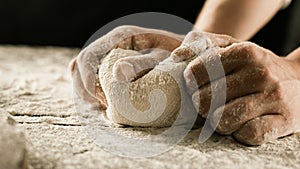 Male chef hands knead dough with flour on kitchen table