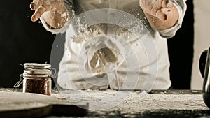 Male chef hands knead dough with flour on kitchen table