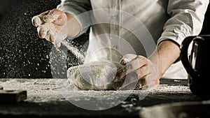 Male chef hands knead dough with flour on kitchen table