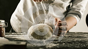 Male chef hands knead dough with flour on kitchen table