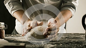 Male chef hands knead dough with flour on kitchen table