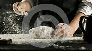 Male chef hands knead dough with flour on kitchen table