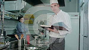 Male chef holding recipe book while cook trainee nodding his head approvingly