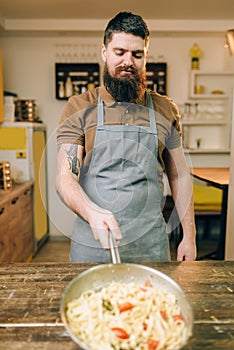 Male chef holds pan with pasta, fettuccine cooking