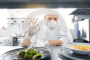 Male chef in mask with food at restaurant kitchen