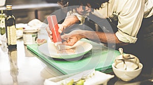 Male chef prepare fish dish for dinner - Man garnishing a starter inside restaurant kitchen - Focus on hands - Exclusive cuisine,