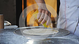 A male chef prepares Focaccia in a restaurant. Greases the rolled dough with oil.