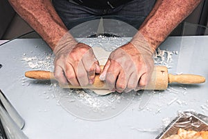 Male chef rolling out pizza dough on a kitchen table