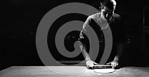 A male chef rolls out thin pizza dough on a table in a pizzeria. Banner and black background