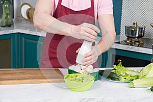 Male chef salting vegetable salad. Cook adding salt to salad with mushrooms and paprika. Man at kitchen preparing dinner.