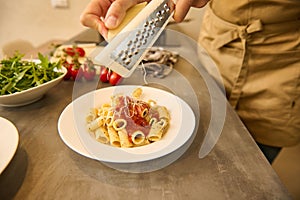 Male chef seasoning Italian pasta with grated cheese. Food background. Culinary. Epicure. Cooking. photo