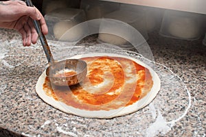 Male chef smears red sauce spicy pizza. Raw dough preform. Production and delivery of pizza